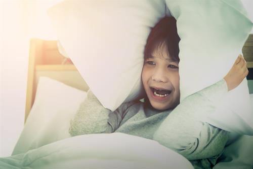 boy-covering-ear-with-pillow-after-waking-up-from-nightmare