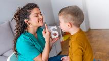Speech therapist with little boy signaling sound of S